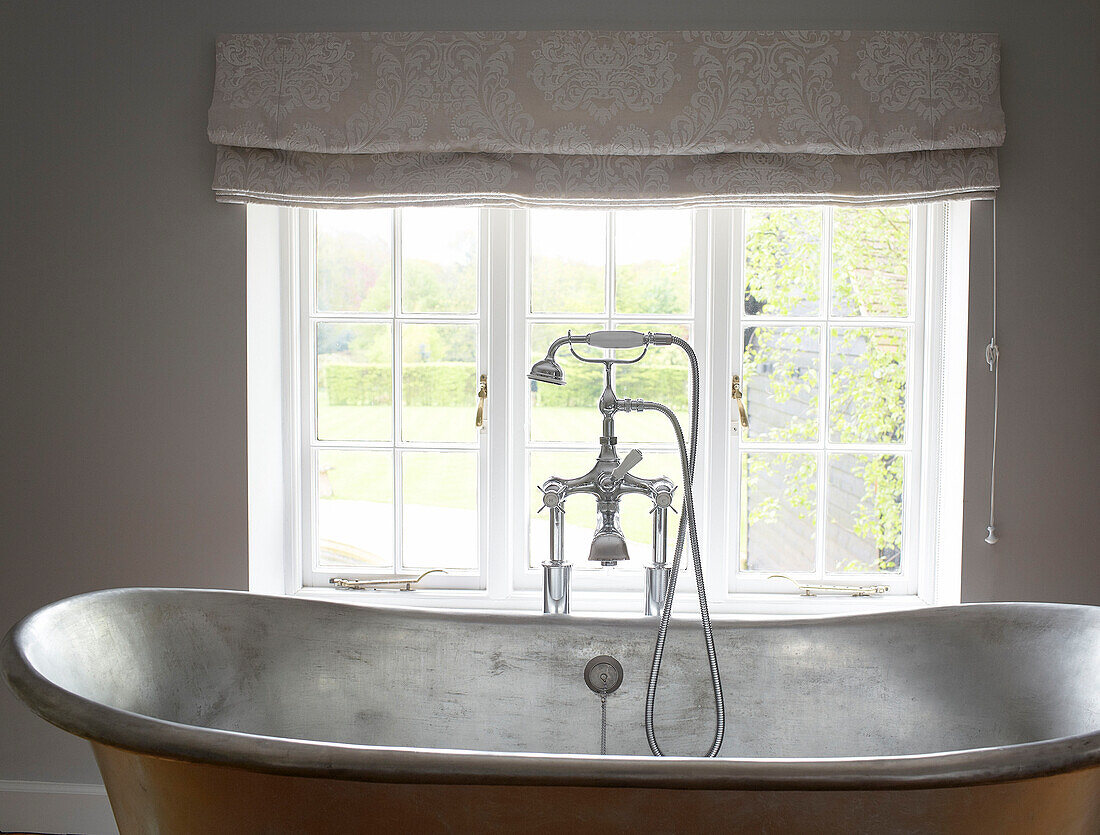 Duscharmatur auf einer freistehenden Metallbadewanne am Fenster eines Hauses in Buckinghamshire, UK