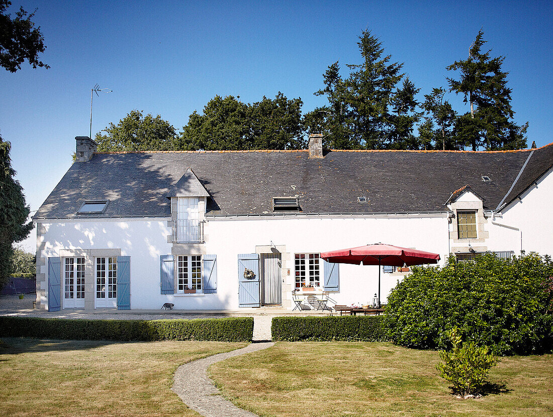 Red parasol on terrace of whitewashed Brittany farmhouse with blue shutters France