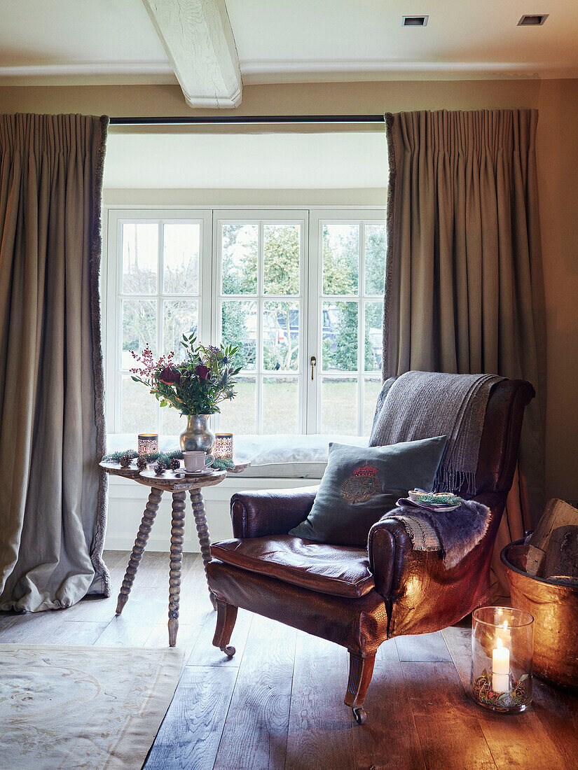 Lit candle and leather armchair with side table in window of Oxfordshire home England UK