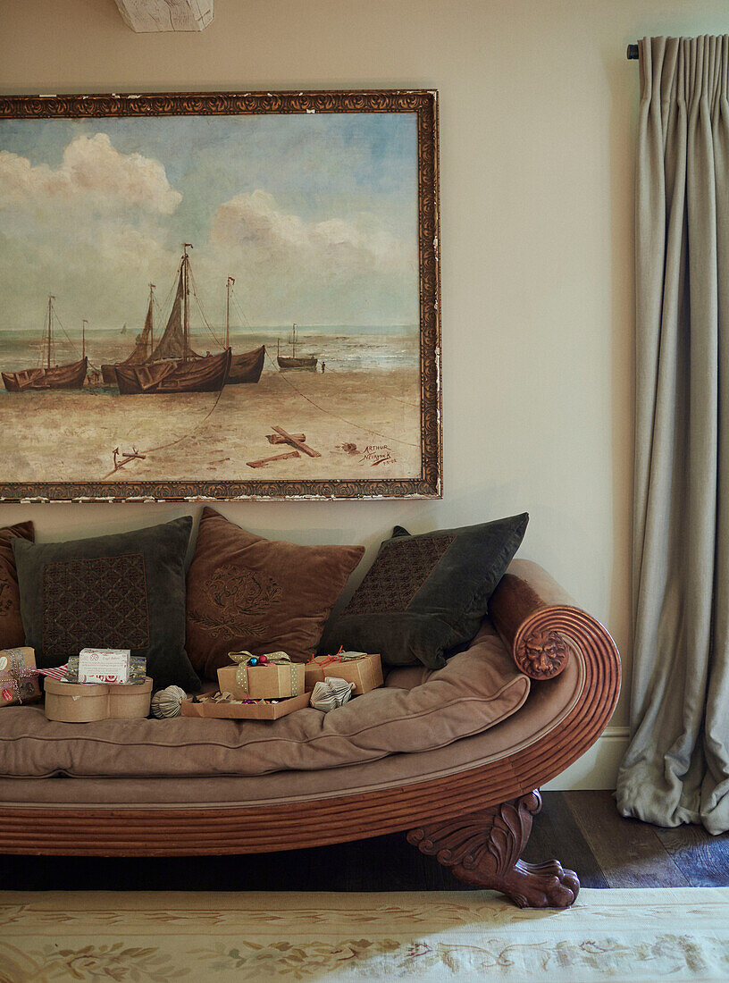 Gift-wrapped presents on antique wooden sofa below framed artwork in Oxfordshire home England UK