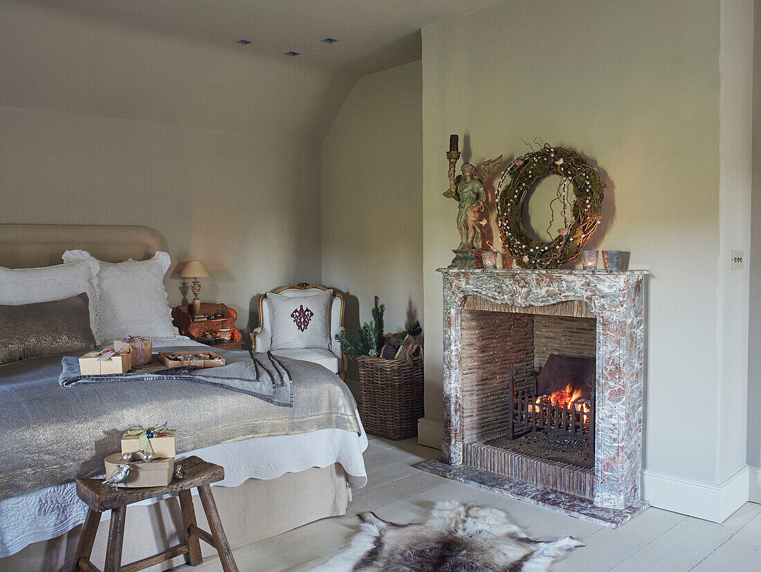 Kranz über angezündetem Feuer mit in braunes Papier eingewickelten Geschenken auf silbernem Bettbezug im Schlafzimmer in Oxfordshire, England, UK
