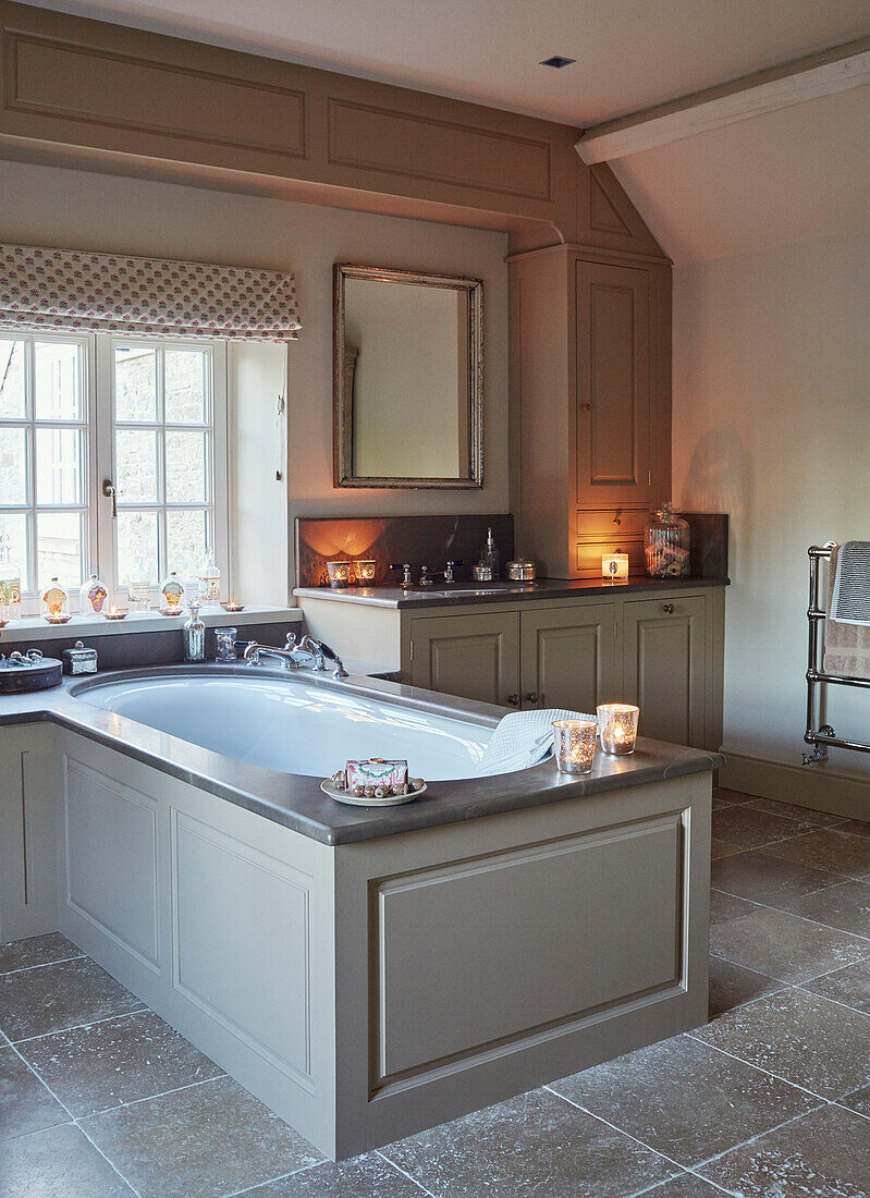 Badewanne mit Einfassung unter dem Fenster mit Raffrollos in einem Haus in Oxfordshire, England, UK