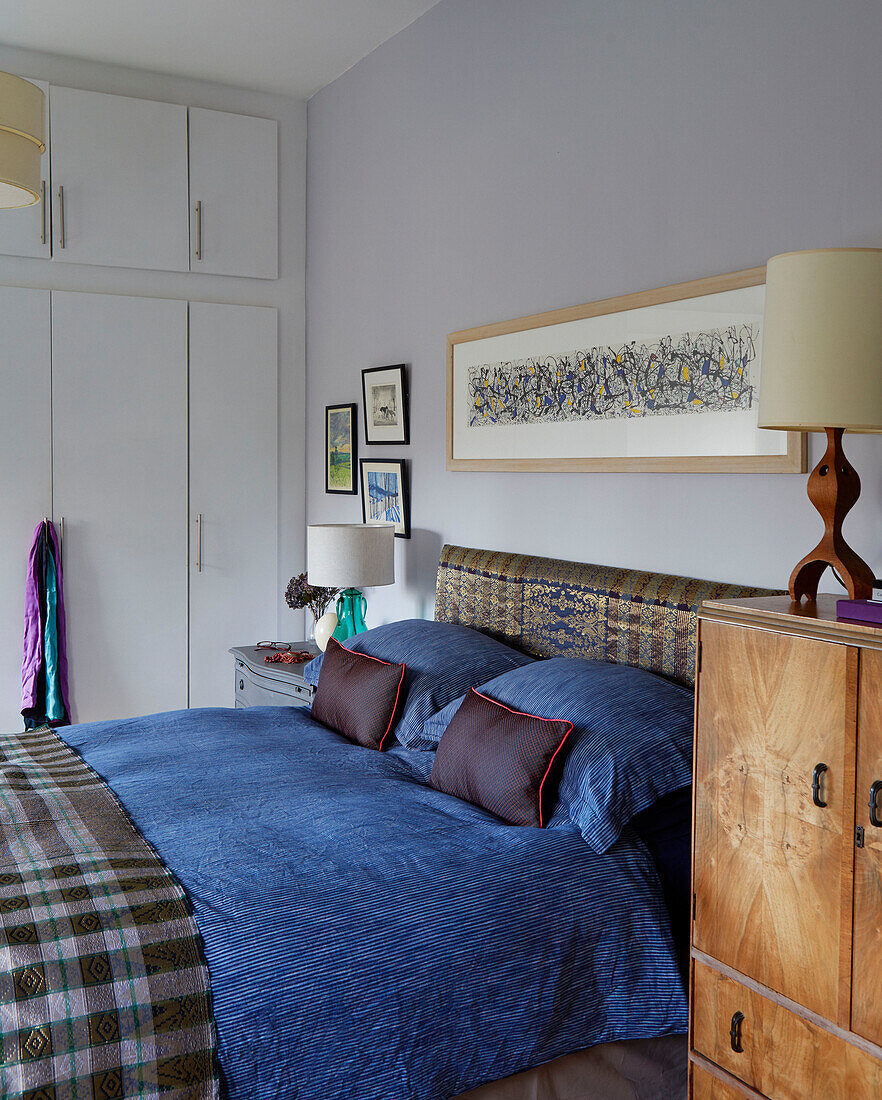 Blau gestreifte Bettdecke auf Doppelbett mit gerahmtem Kunstwerk und Retro-Lampe in einem Haus in Speldhurst, Kent, England