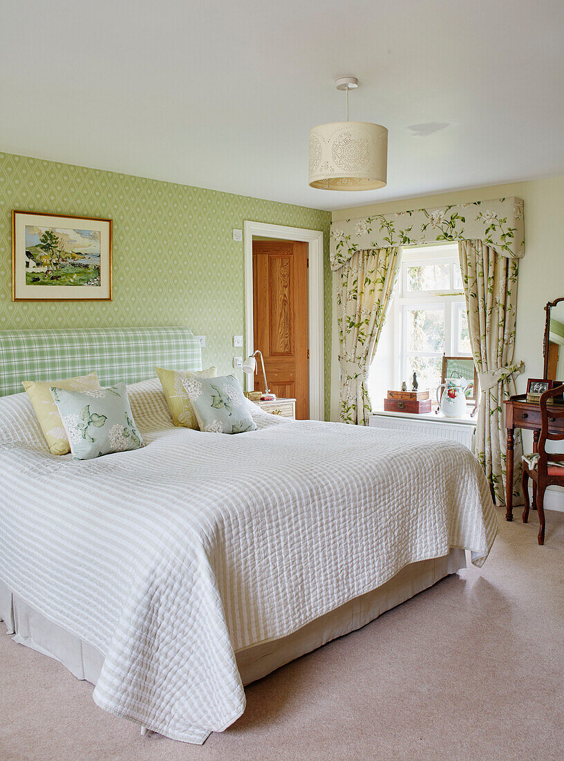 Grüne geblümte Vorhänge und Tapeten mit Gingham-Kopfteil in einem Schlafzimmer in einem Bauernhaus in Hexham, Northumberland, Großbritannien