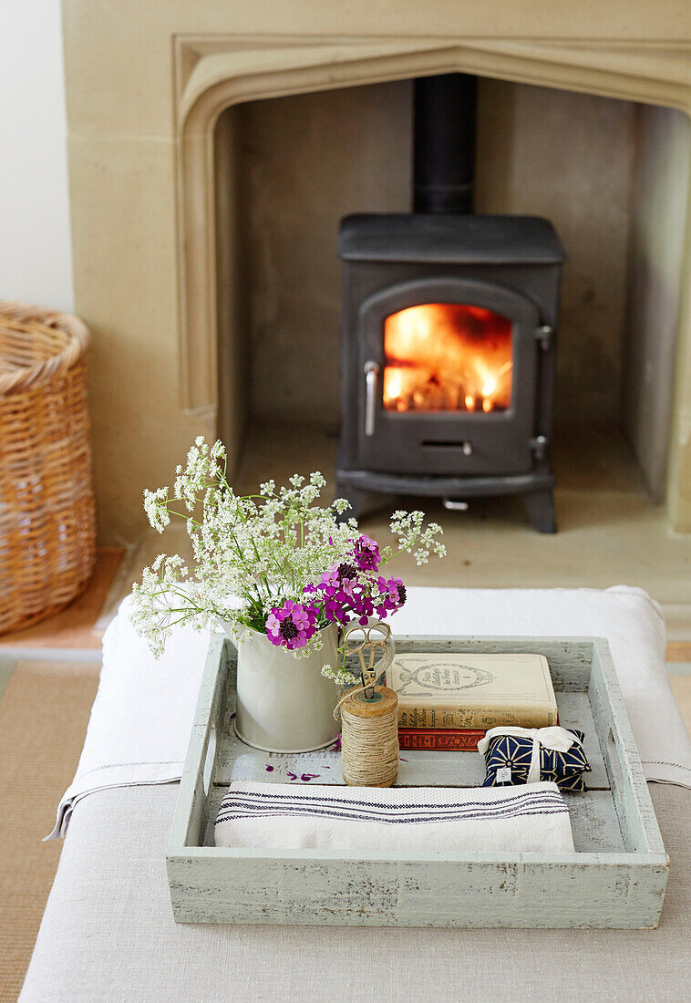Cut flowers on tray with lit woodburner in Northumbrian home England UK