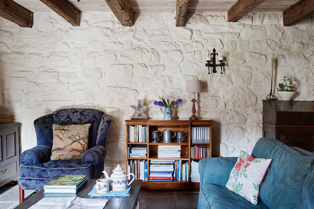 Blue armchair and sofa with bookcase set against whitewashed wall in Grade II listed Tudor bastle Northumberland UK