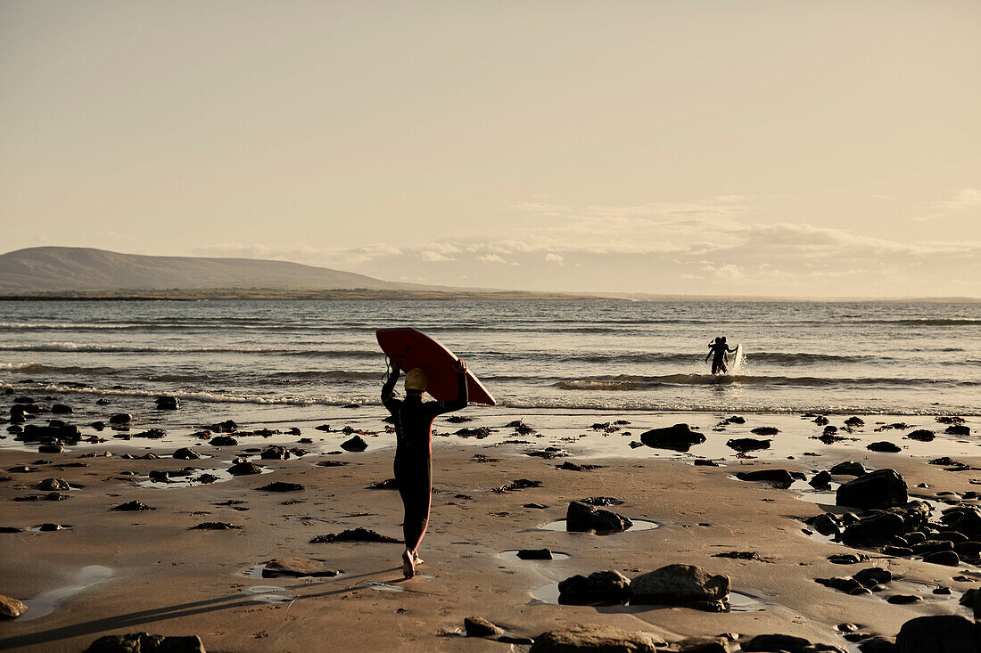 Jungen tragen Bodyboards ins Meer an der Küsten der Grafschaft Sligo in Connacht, Irland