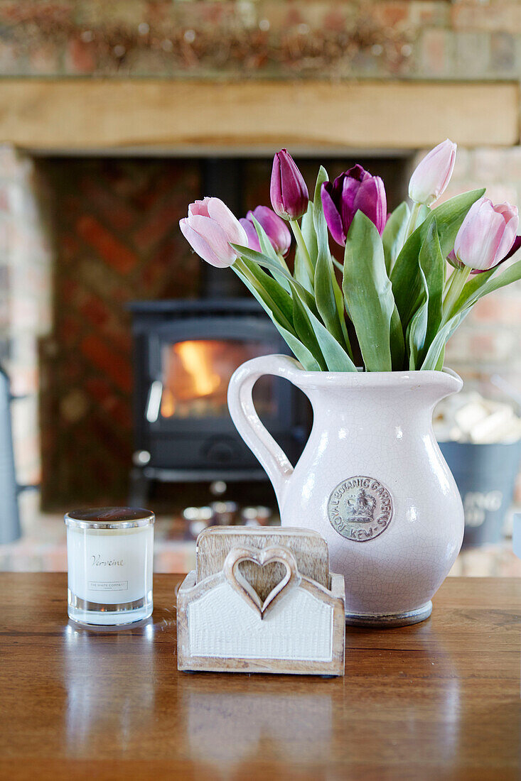 Cut tulips in ceramic jug with lit woodburner in County Durham cottage, England, UK
