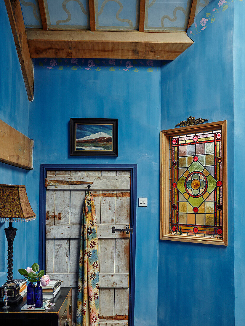 Buntglasfenster in blauem Raum mit Stoffbehang an der Rückseite der Tür in einem Bauernhaus in Herefordshire, UK