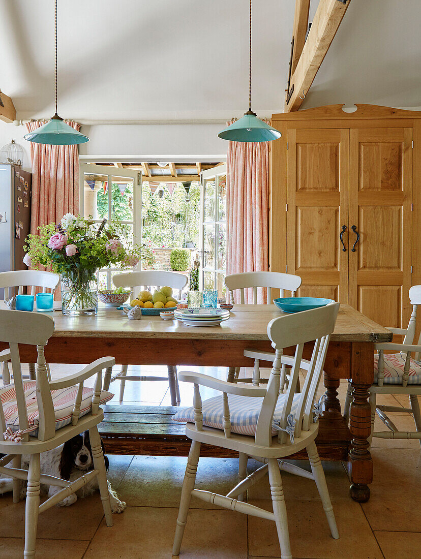 Dining table with painted chairs and wooden cabinet in Warwickshire farmhouse, UK