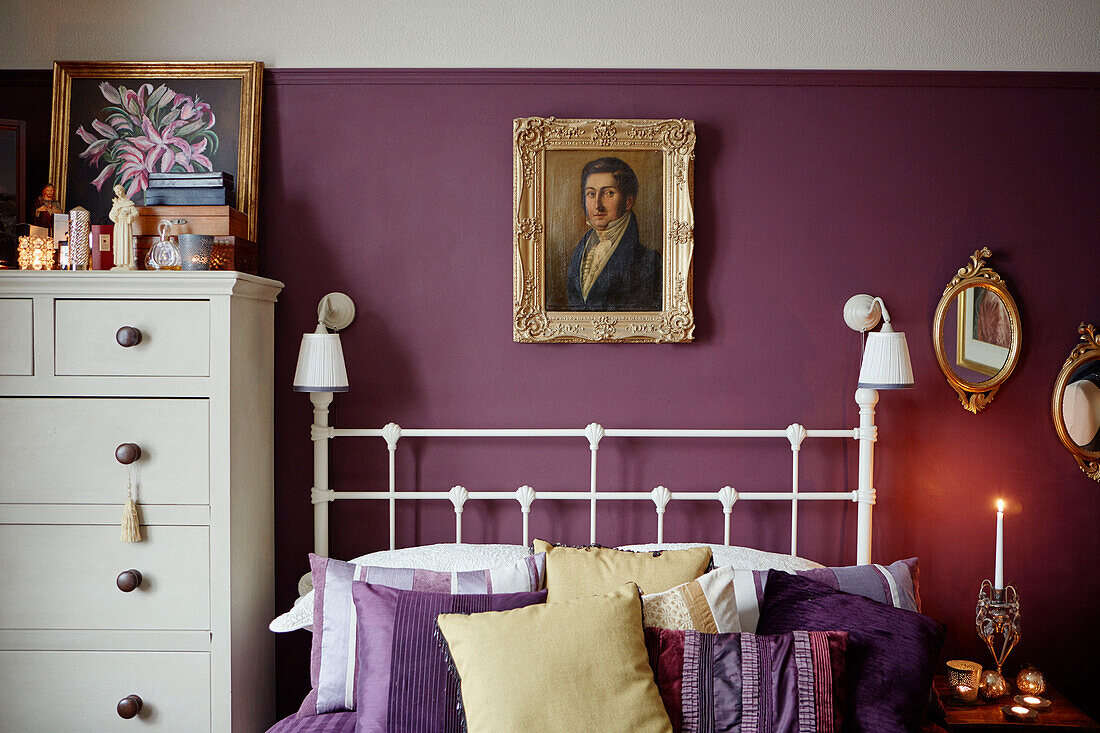 Gilt framed portrait above white double bed with cushions in purple Chippenham bedroom, Wiltshire, UK
