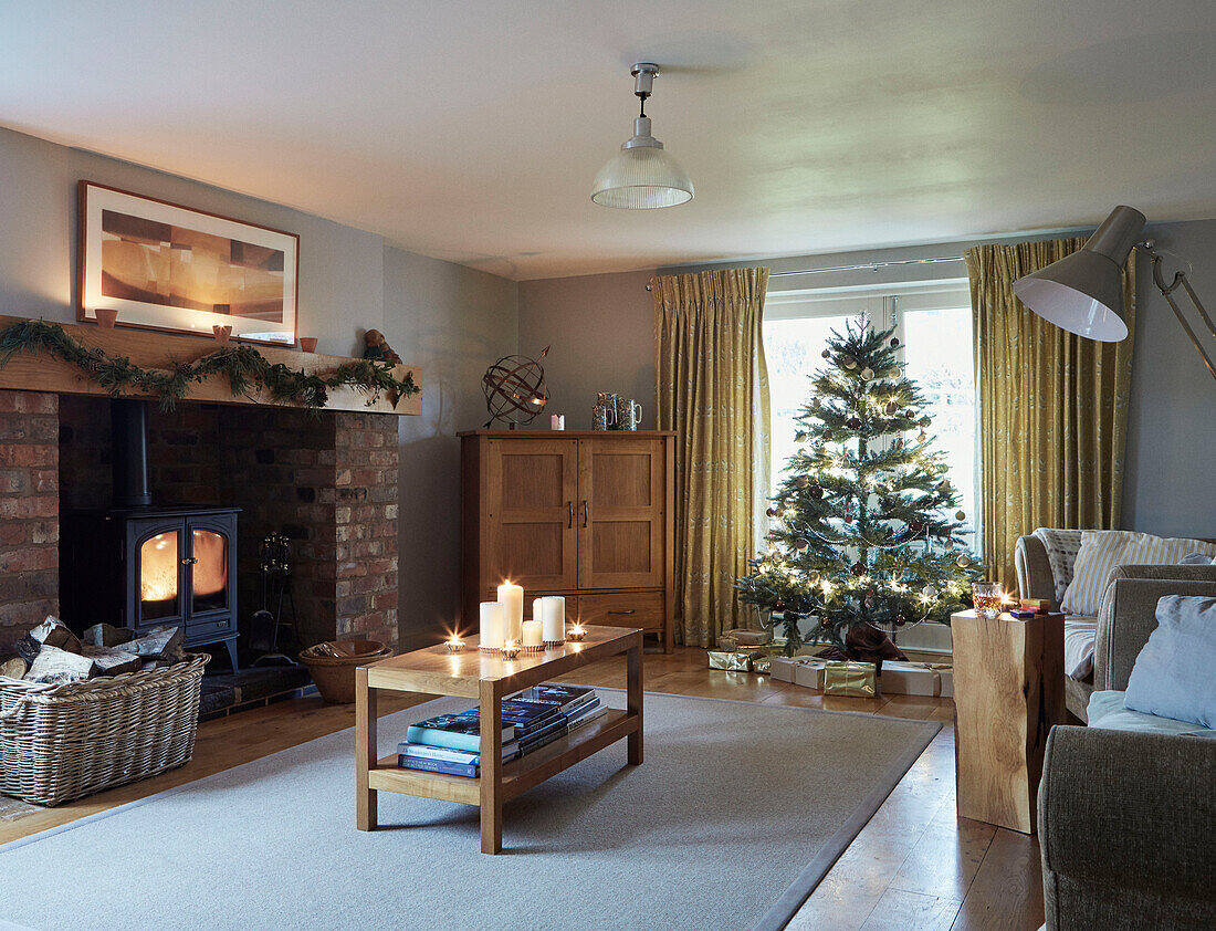 Couchtisch aus Holz mit beleuchtetem Holzofen und Weihnachtsbaum im Wohnzimmer in Worcestershire, England, UK