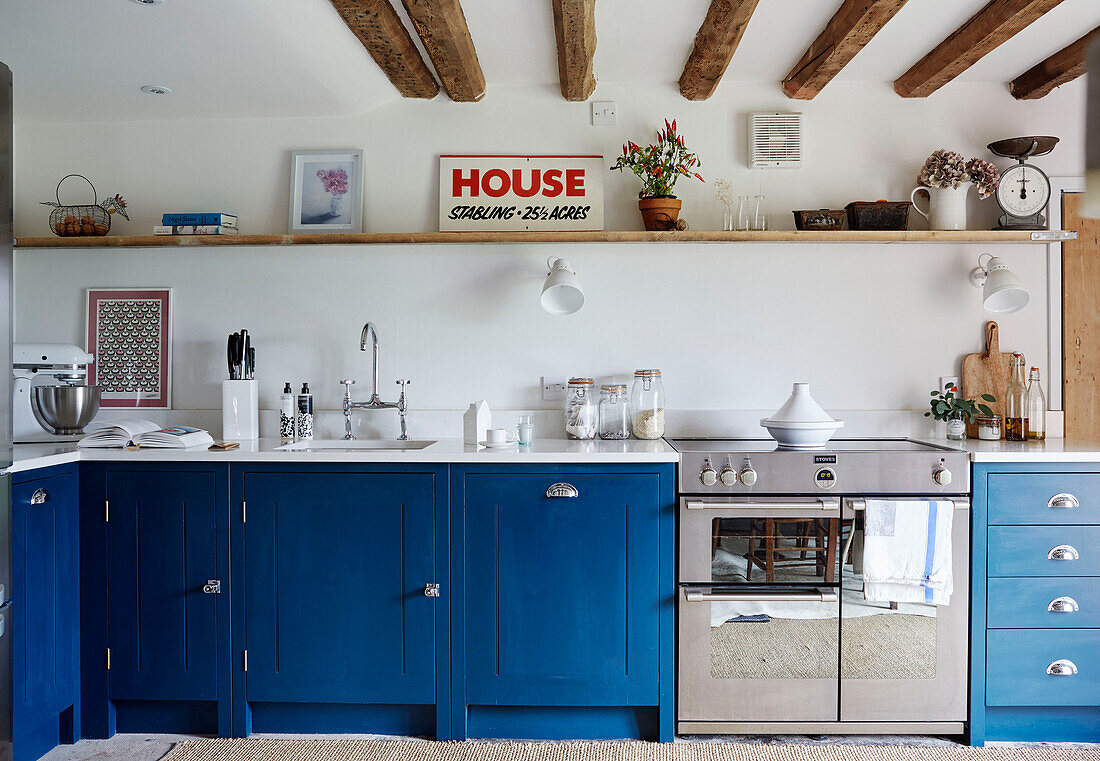 Blue fitted units with shelf under beamed ceiling in Warwickshire farmhouse, England, UK