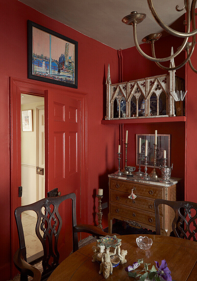 Esszimmer mit offener Tür, Kommode, Tisch und Stühlen mit Metallkronleuchter in rotem georgianischem Esszimmer aus dem 19. Jahrhundert Talgarth, Mid Wales, UK
