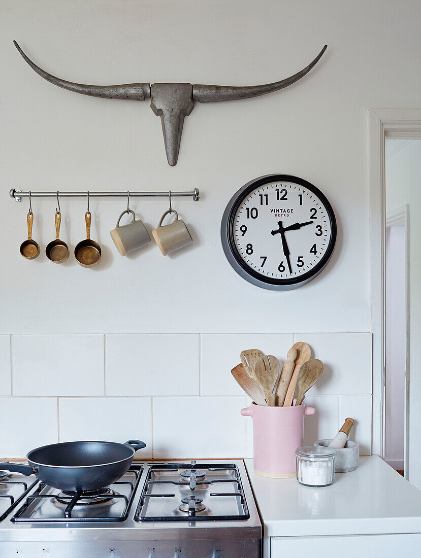 Metallgeweih und Uhr über Küchenutensilien mit Pfanne auf Gaskochfeld in einem Haus in Tunbridge Wells, Kent, UK