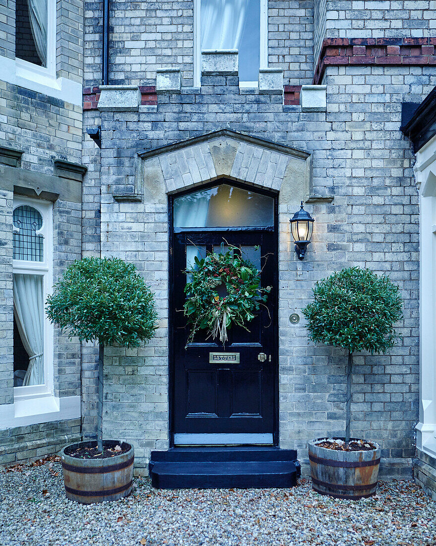 Weihnachtskranz an schwarzer Haustür eines britischen Hauses mit gepflanzten Bäumen