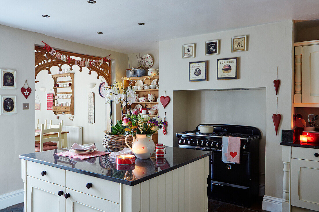 Blumen auf einer Kücheninsel mit Herzdekoration und Girlande in einer weihnachtlichen weißen Einbauküche in einem britischen Haus