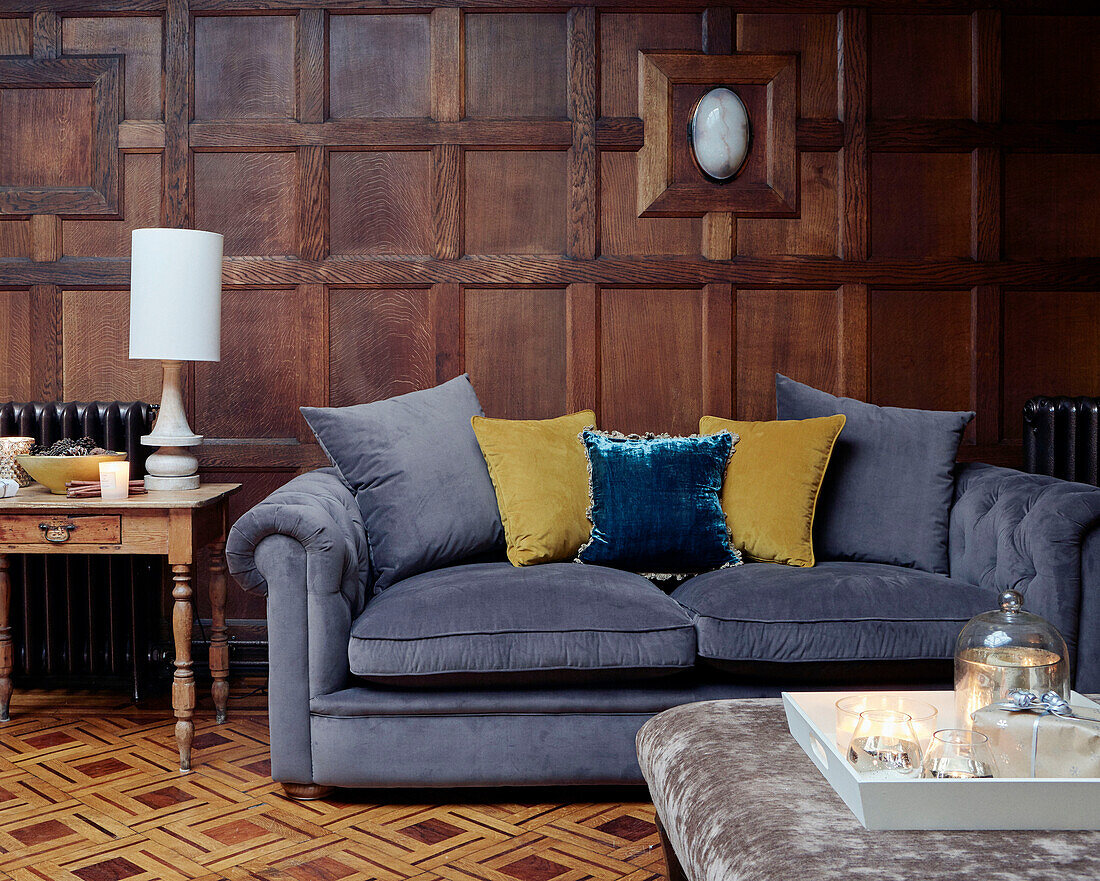 Gelbe Kissen auf grauem Samt-Chesterfield im holzgetäfelten Wohnzimmer eines britischen Hauses
