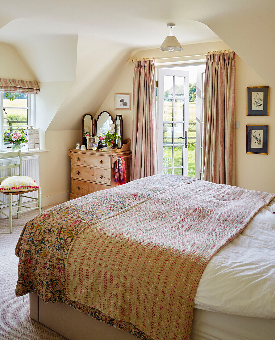Gemusterte Bettdecke und Holztruhe mit offener Tür in einem Cottage in Sandford St Martin, Oxfordshire, UK