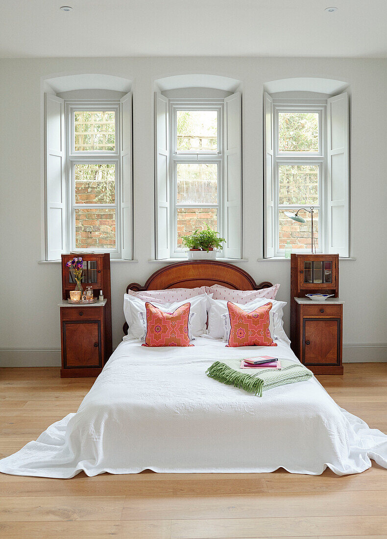 Niedriges Doppelbett mit Holzschränken unter dem Dreifachfenster in Woodstock home Oxfordshire, UK