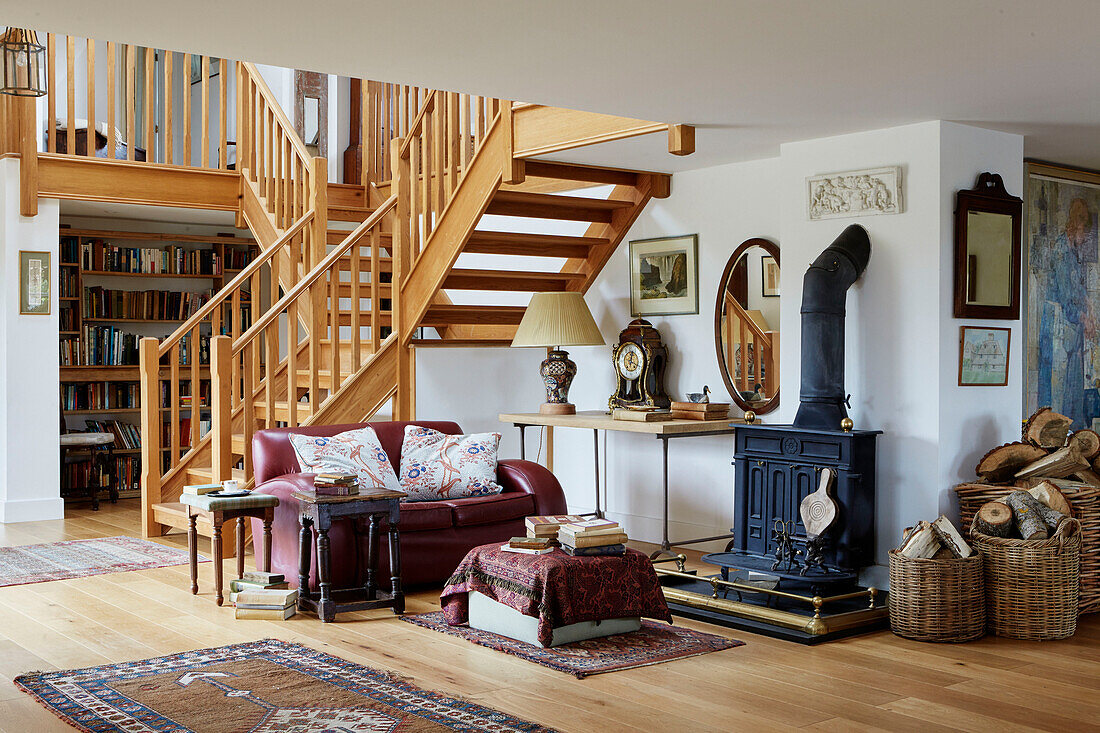 Red leather sofa and woodburner below open tread stairs in open plan Oxfordshire home, UK