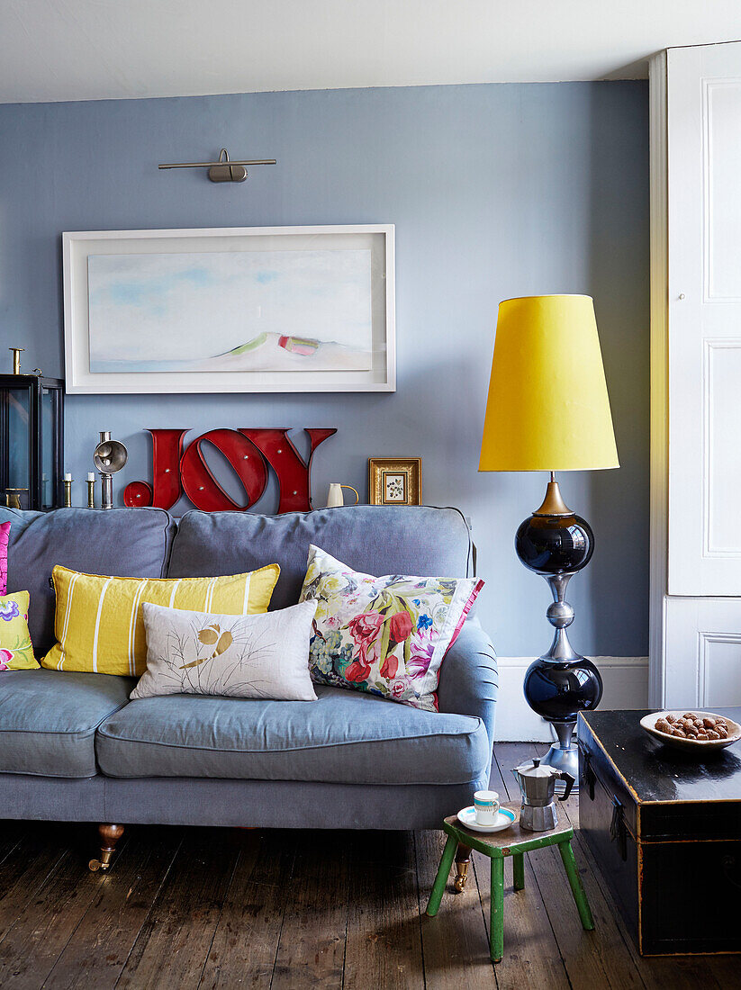 Große Retro-Lampe und Sofa mit Kunstwerken und dem Wort JOY" in einem Haus in Deddington, Oxfordshire, UK"