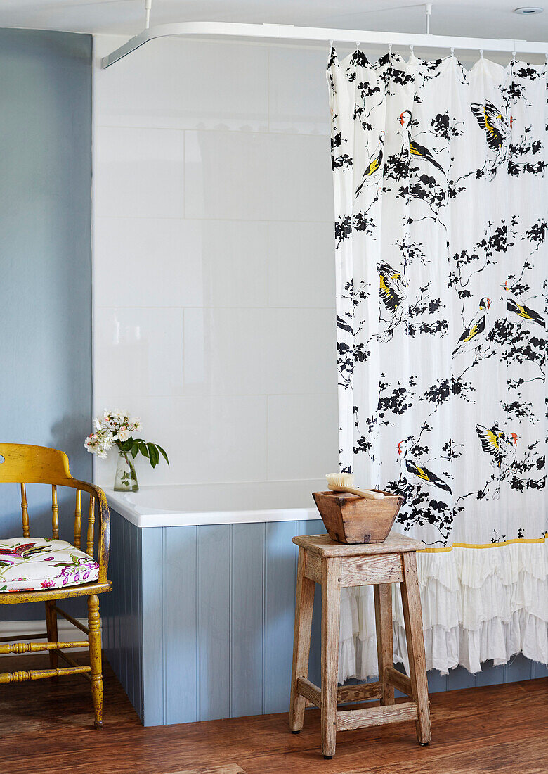 Gemusterter Duschvorhang und Holzhocker mit blau getäfelter Badewanne in einem Haus in Deddington, Oxfordshire, UK