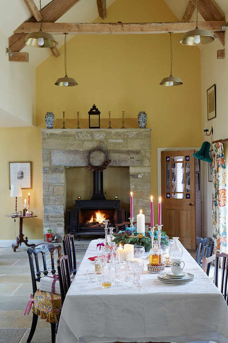 Dining table and lit woodburning stove in double height Northumberland farmhouse, UK