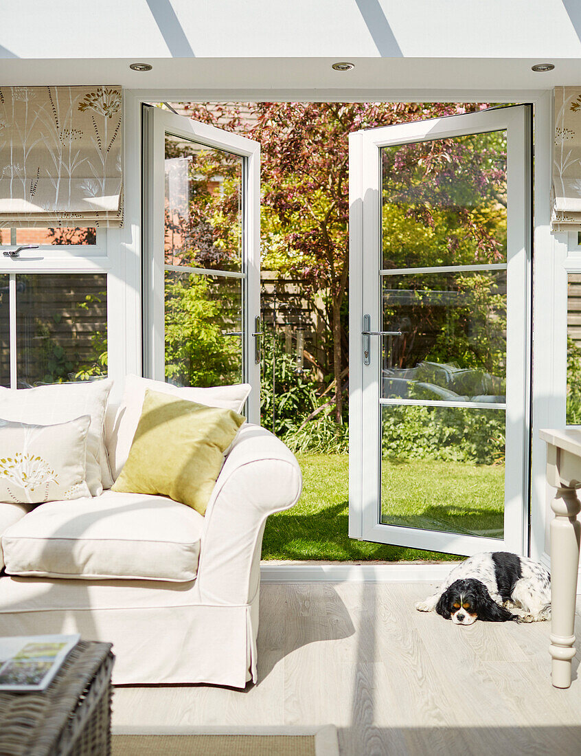 White sofa with open garden doors to garden in North Yorkshire conservatory, UK