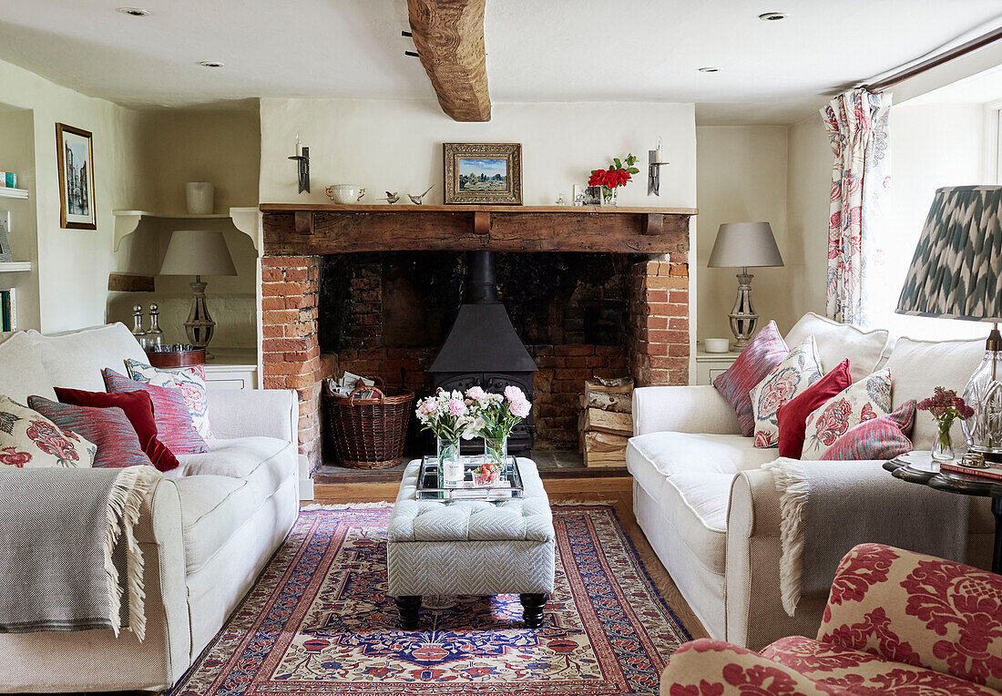Weiße Sofas mit roten Samtkissen und offenem Ziegelsteinkamin in einem Ferienhaus in Berkshire, England, UK