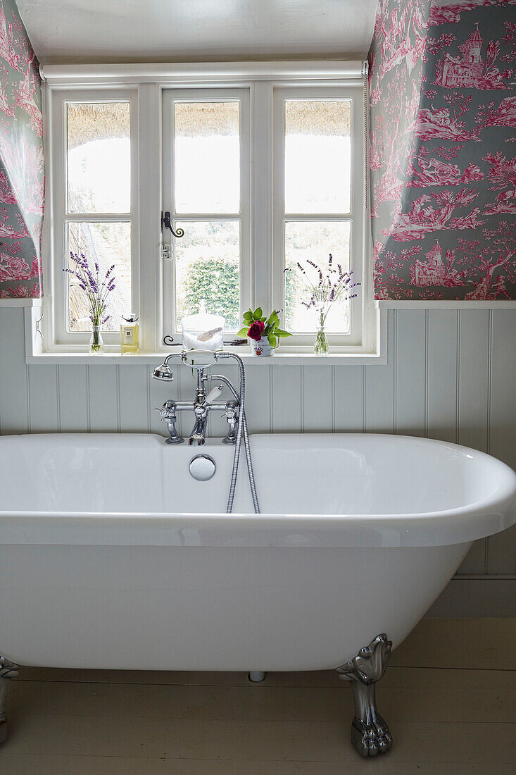 Weiße freistehende Badewanne unter einem Fenster in einem Landhaus in Berkshire, England, UK
