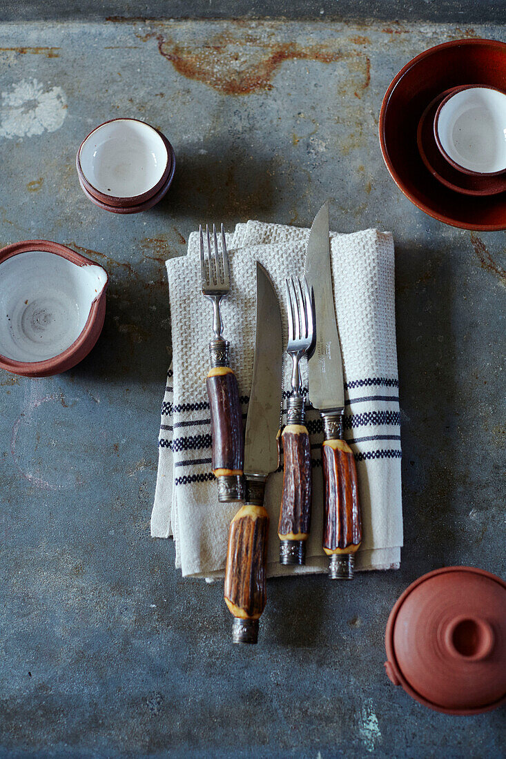 Rustic wooden handled cutlery on dishcloth with ceramic bowls in Brittany cottage, France