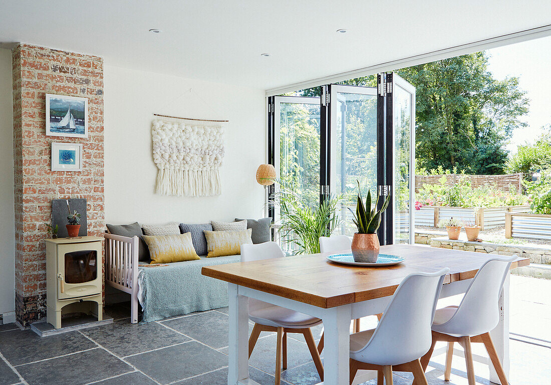 Dining table and chairs with daybed and open doors to garden in Bath home, Wiltshire, UK