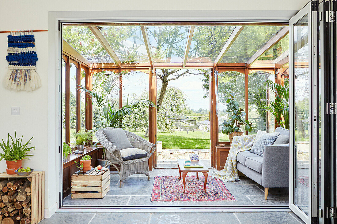 Wicker chair and grey sofa in wooden conservatory extension of Bath home, Wiltshire, UK