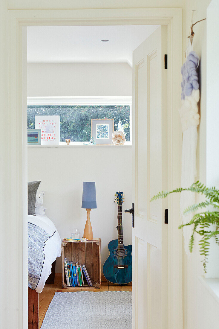 Blick durch die offene Tür auf eine Kiste und eine Gitarre am Bett im Zimmer eines Teenagers in Bath, Wiltshire, UK