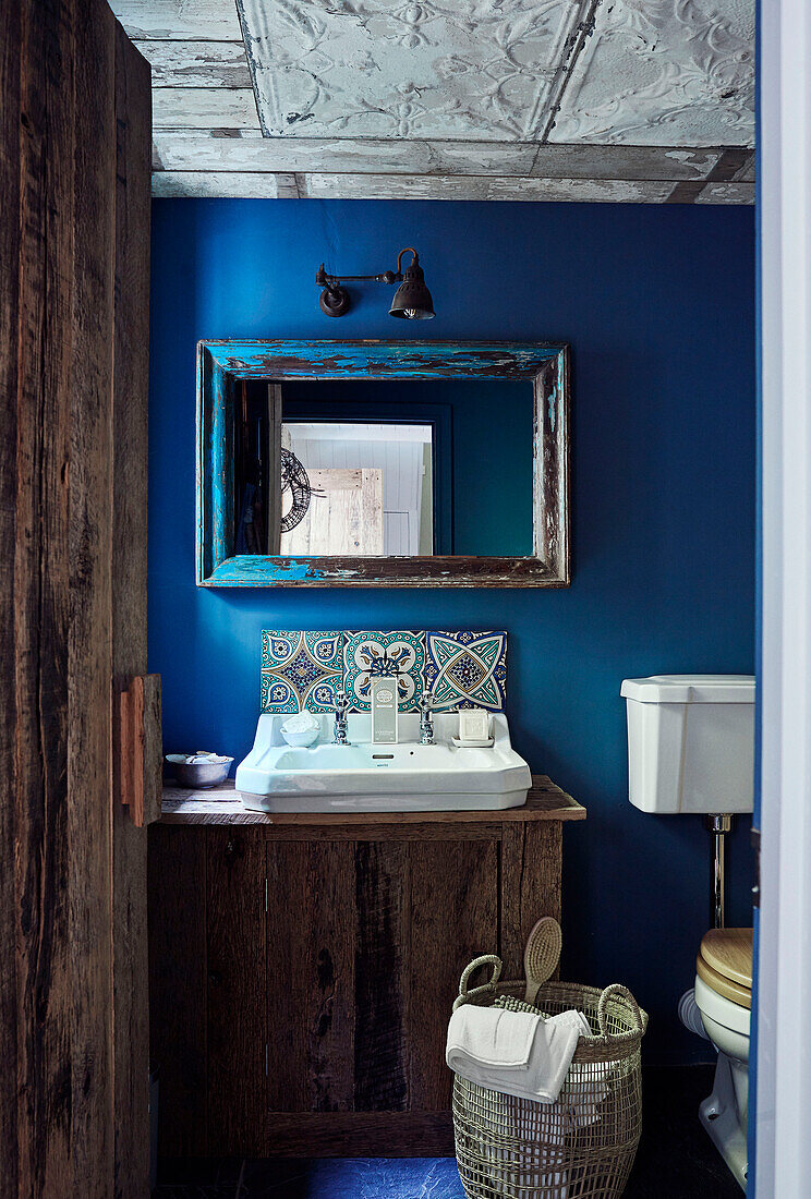 Blick durch eine Holztür in ein hellblaues Badezimmer mit Spiegel in einem Haus in Devon, England