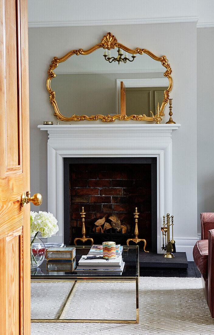 Gilt framed mirror above fireplace with glass coffee table in Durham home, England, UK