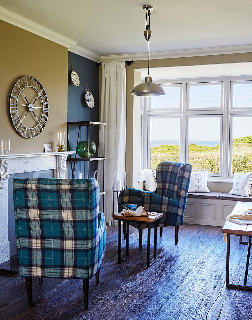 Ein Paar karierte Sessel und eine Uhr mit Blick auf das Meer in einem Haus an der Küste von Northumbria, UK
