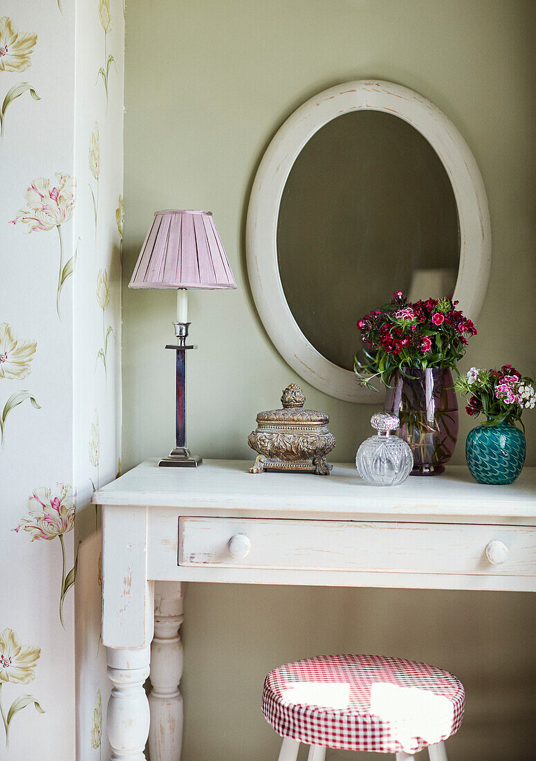 Ovaler Spiegel mit Schnittblumen und Parfümflaschen in einem Cottage in den Cotswolds, UK