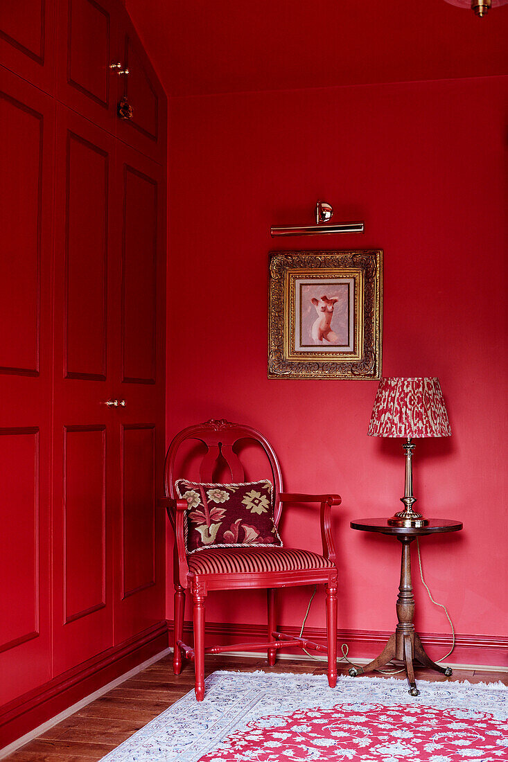 Lampe auf Beistelltisch mit rotem Stuhl und Schränken und vergoldetem gerahmten Bild in einem Cottage in den Cotswolds, UK