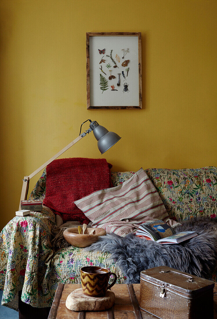 Gerahmte Fundstücke über dem Sofa mit bestickter Decke in einem Cottage in Gladestry an der Grenze zu Südwales