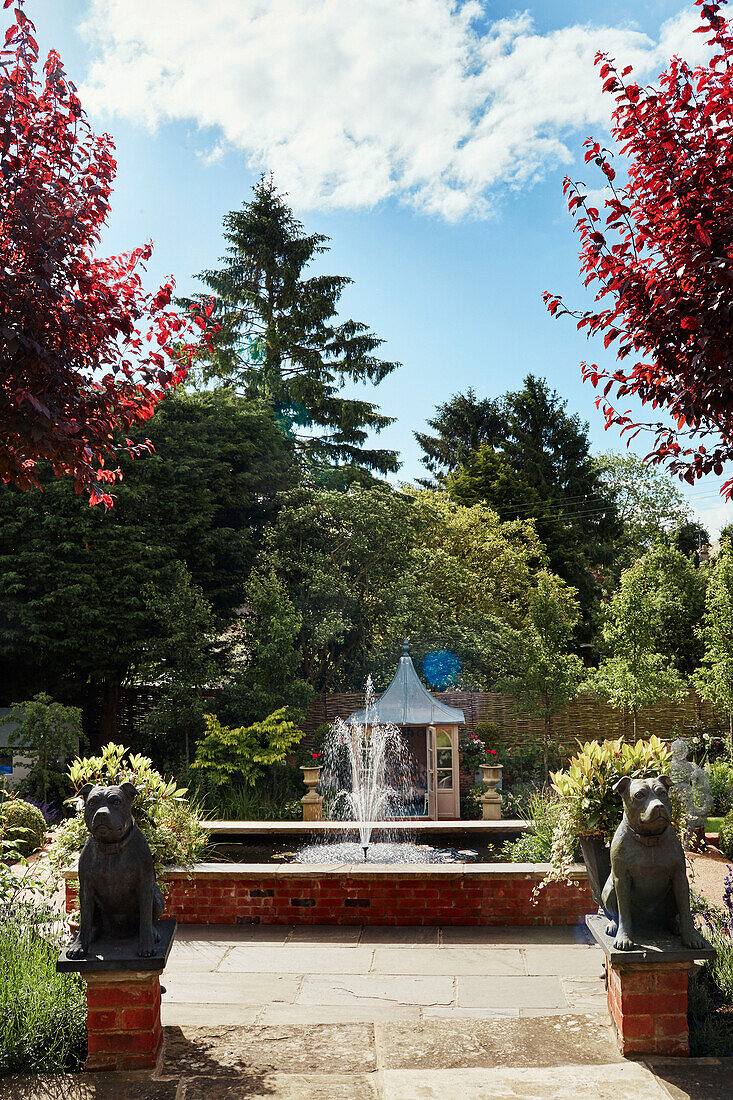 Wasserfontäne und Hundestatuen in einem Garten in den Cotswolds, UK