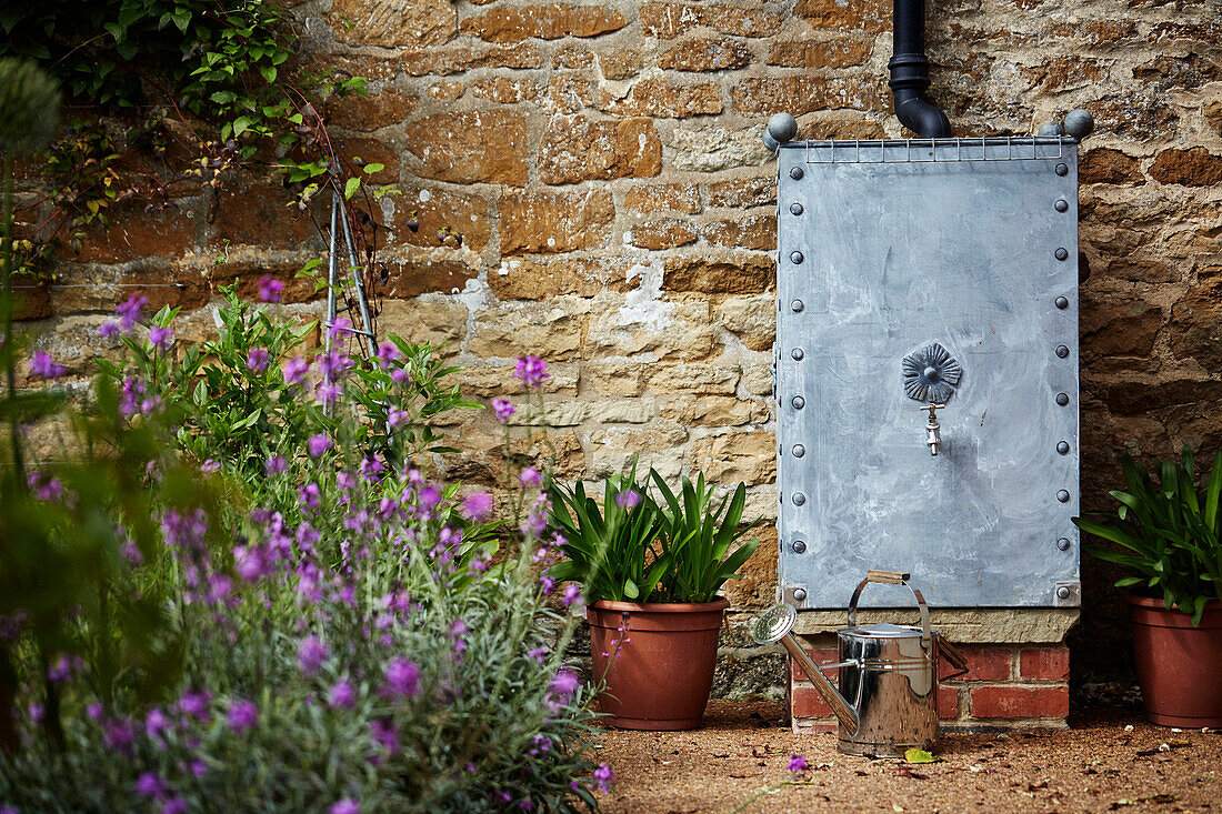 Metall-Wassertonne im Garten eines Steinhauses in den Cotswolds, UK