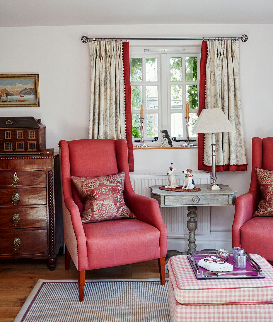 Ein Paar rote Sessel und eine Holzkommode am Fenster in einem Cottage in den Cotswolds, UK