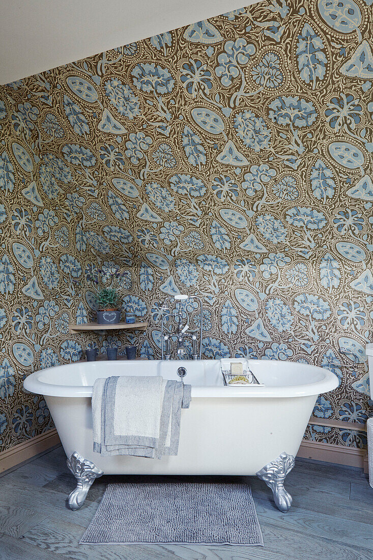 Freistehende Krallenfußbadewanne mit blau-goldener Mustertapete in einem Cottage in den Cotswolds, UK