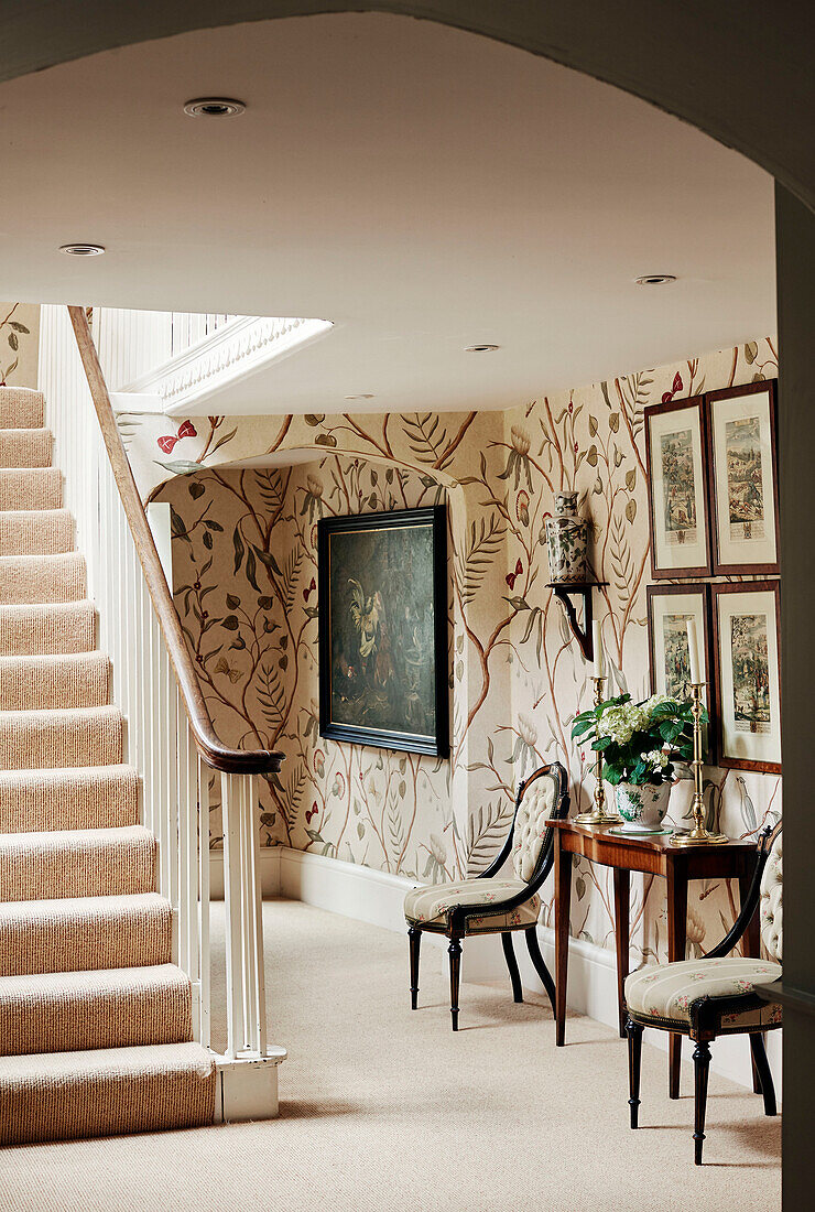 Floral wallpaper and chairs with console in hallway of Cotswolds home, UK