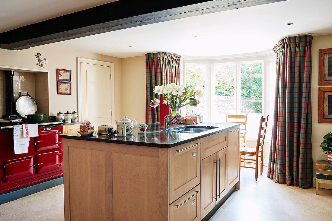 Kitchen island and red stpve with daylight in bay window of Cotswolds home, UK