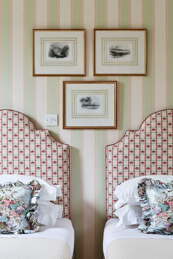 Framed prints above twin beds with floral cushions in Cotswolds home, UK