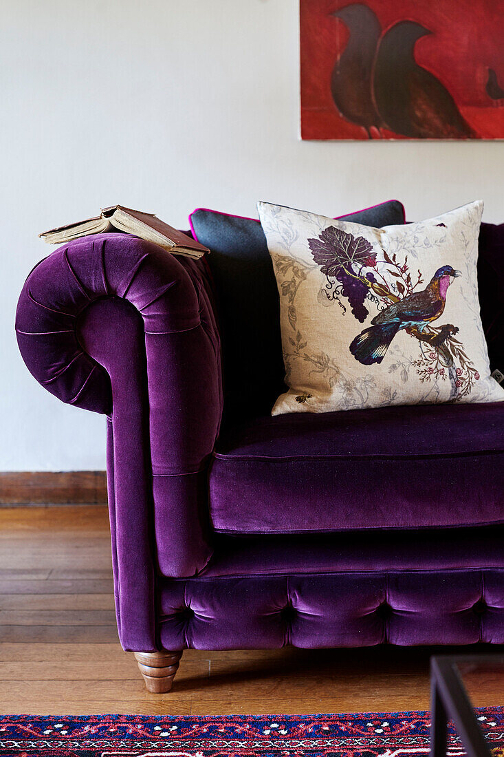Kissen mit Vogelmotiv auf lila geknöpftem Sofa und Kunstwerk in einem Haus in Devon, UK