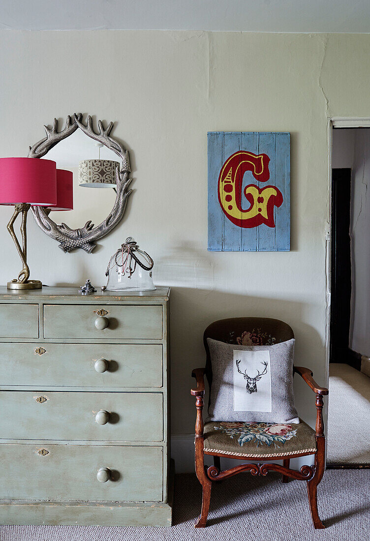 Pinkfarbene Lampe und Spiegel mit Kommode und Kunstwerk mit dem Buchstaben 'G' in einem Haus in Devon, UK